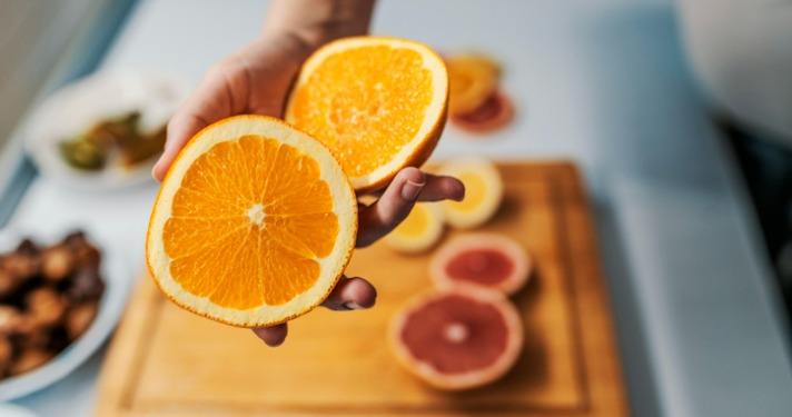 Female hand holding fresh Orange in her kitchen. Home grown ripe clementines, organic food that the girl holds in her hand. Woman holding two halves of Orange citrus fruit Vitamin C article image